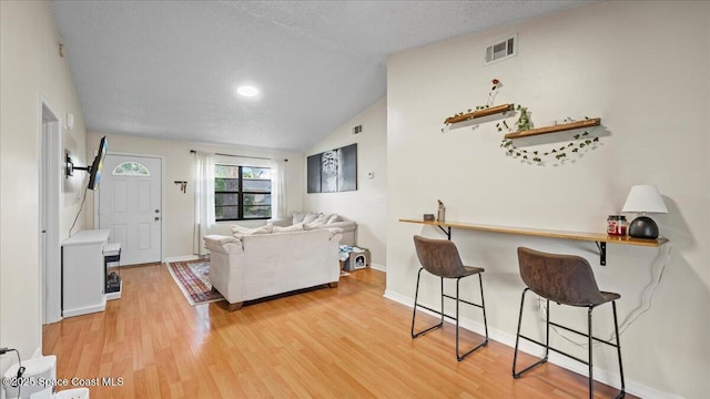 living room with lofted ceiling, light hardwood / wood-style flooring, and a textured ceiling