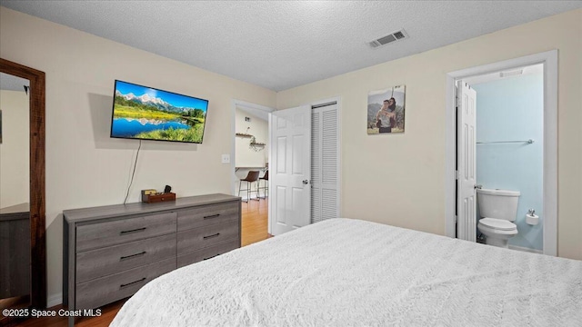 bedroom featuring hardwood / wood-style flooring, ensuite bath, a closet, and a textured ceiling