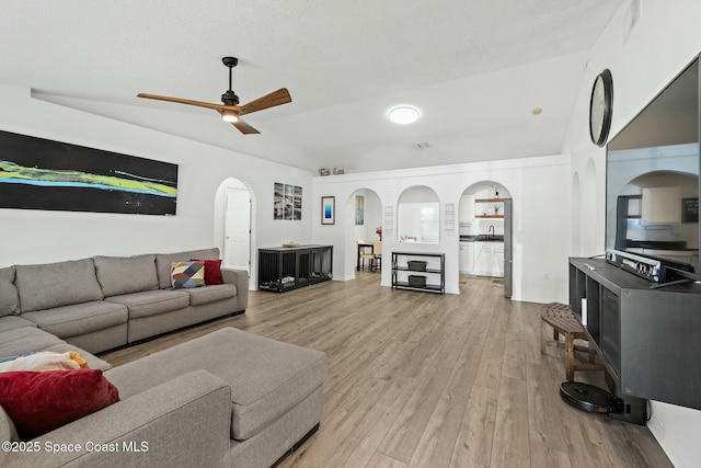 living room with lofted ceiling, a textured ceiling, ceiling fan, and light wood-type flooring