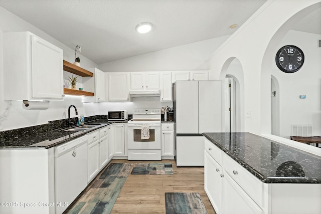 kitchen with sink, white appliances, dark stone countertops, white cabinets, and vaulted ceiling