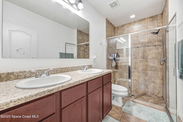 bathroom with tile patterned floors, toilet, a textured ceiling, vanity, and a shower with door