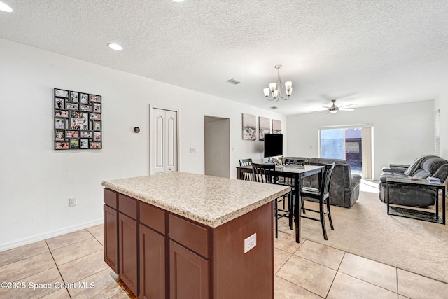 kitchen with pendant lighting, a kitchen island, a textured ceiling, light tile patterned flooring, and ceiling fan with notable chandelier