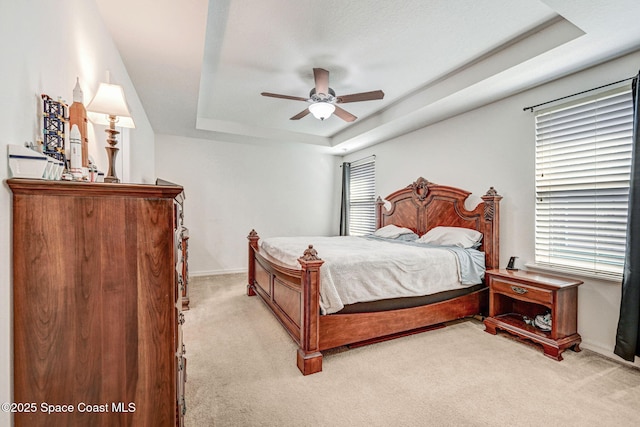 carpeted bedroom with a raised ceiling, ceiling fan, and multiple windows