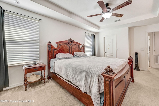 bedroom with ceiling fan, a tray ceiling, and light carpet