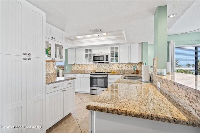 kitchen featuring sink, appliances with stainless steel finishes, white cabinetry, light stone counters, and a raised ceiling