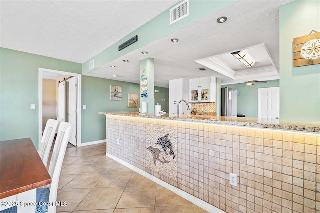 kitchen featuring light tile patterned floors, ceiling fan, a textured ceiling, a raised ceiling, and a barn door