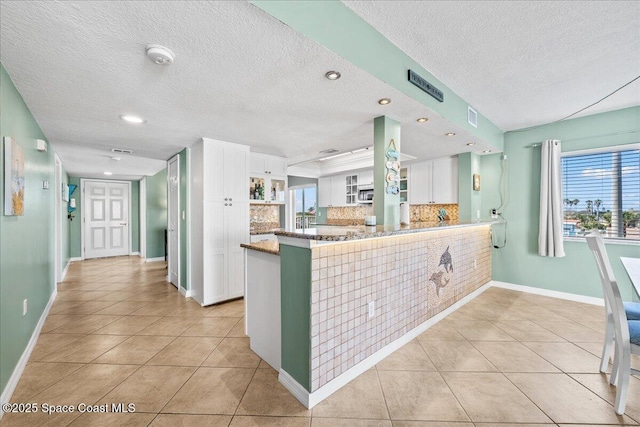 kitchen featuring light tile patterned floors, backsplash, kitchen peninsula, and white cabinets