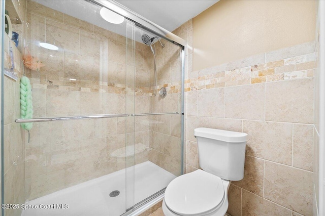 bathroom featuring toilet, an enclosed shower, and tile walls