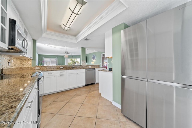 kitchen featuring light tile patterned floors, crown molding, appliances with stainless steel finishes, a tray ceiling, and white cabinets