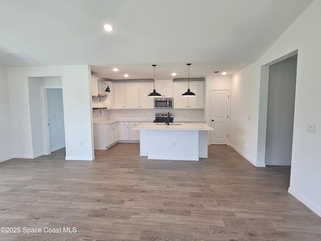 kitchen featuring appliances with stainless steel finishes, white cabinetry, a center island with sink, decorative light fixtures, and light wood-type flooring