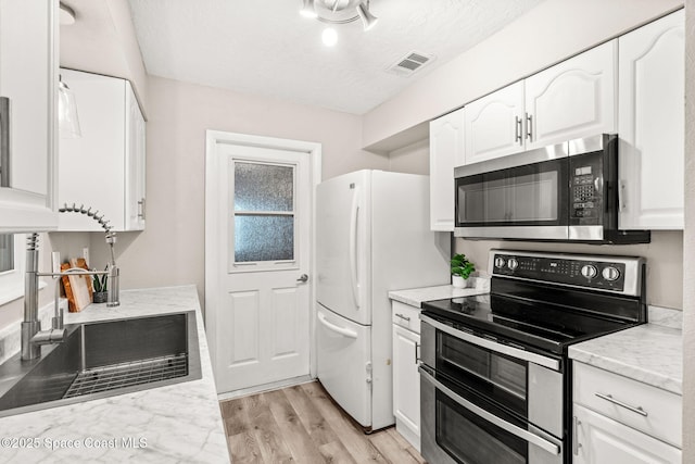 kitchen with sink, appliances with stainless steel finishes, light stone counters, light hardwood / wood-style floors, and white cabinets