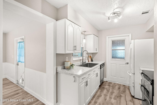 kitchen featuring sink, a textured ceiling, light wood-type flooring, stainless steel appliances, and white cabinets