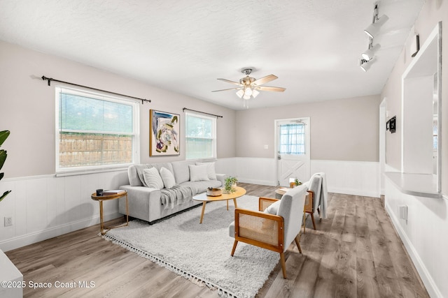 living room with ceiling fan, track lighting, light hardwood / wood-style flooring, and a textured ceiling