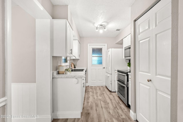 kitchen with white cabinetry, appliances with stainless steel finishes, a textured ceiling, and light hardwood / wood-style floors