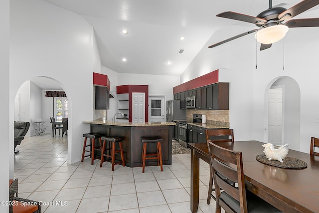 kitchen featuring light tile patterned floors, a breakfast bar area, appliances with stainless steel finishes, decorative backsplash, and kitchen peninsula