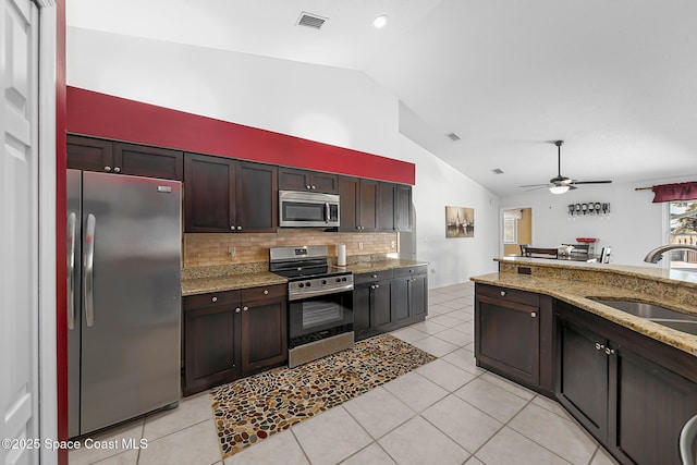 kitchen with sink, appliances with stainless steel finishes, light stone counters, dark brown cabinetry, and vaulted ceiling