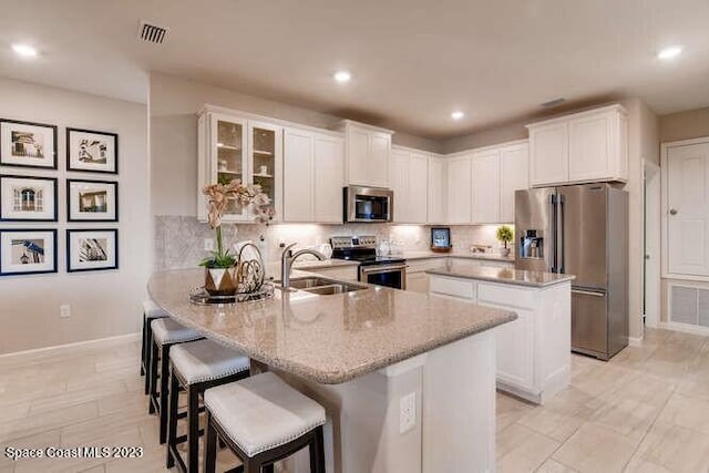 kitchen with white cabinetry, sink, a kitchen bar, stainless steel appliances, and a center island with sink