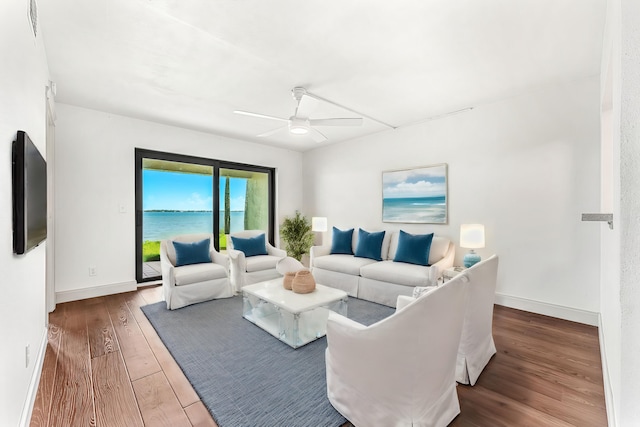 living room featuring dark wood-type flooring, ceiling fan, and a water view