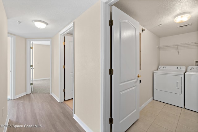 clothes washing area with washer and dryer, a textured ceiling, and light tile patterned floors