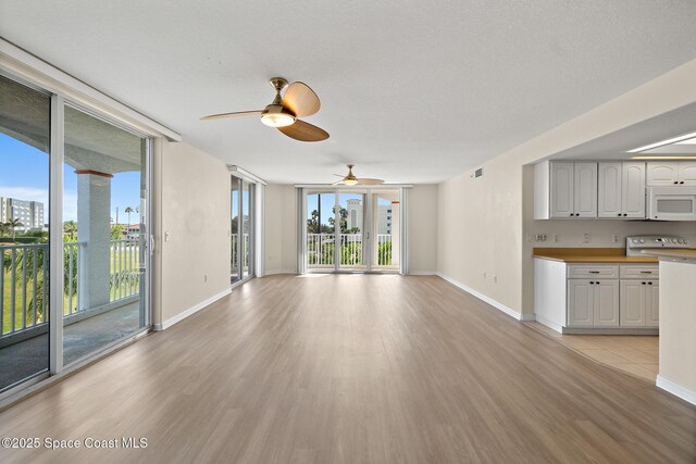 unfurnished living room with ceiling fan, a wall of windows, and light wood-type flooring