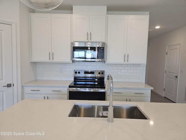 kitchen with appliances with stainless steel finishes, sink, white cabinets, decorative backsplash, and light stone counters