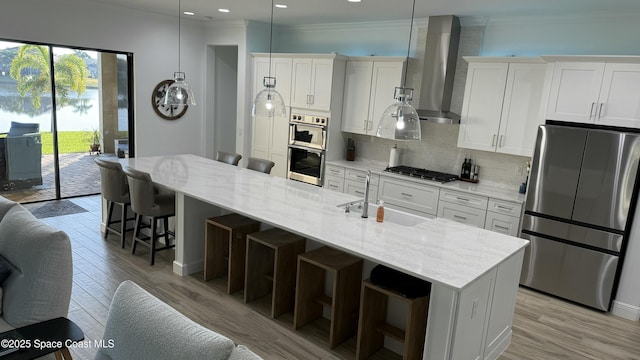 kitchen with a center island with sink, appliances with stainless steel finishes, wall chimney range hood, and white cabinets