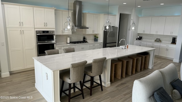 kitchen with a breakfast bar, range hood, an island with sink, and appliances with stainless steel finishes