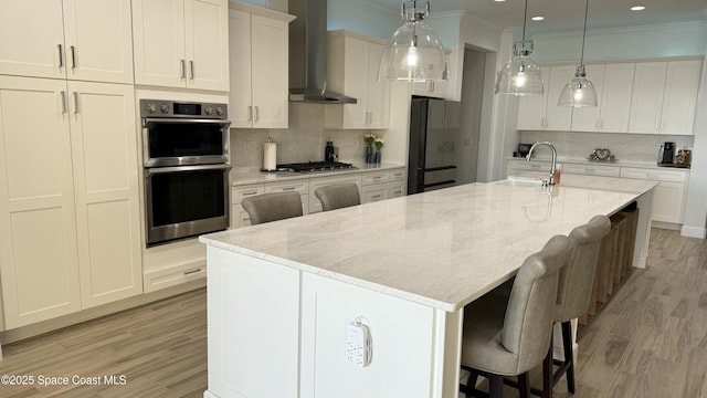 kitchen with a large island with sink, white cabinets, stainless steel appliances, and wall chimney exhaust hood