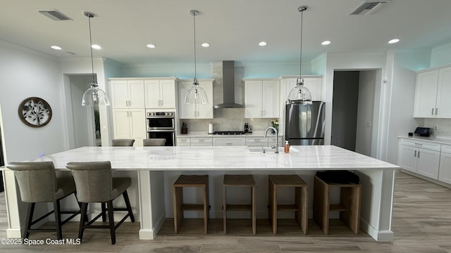 kitchen with a large island, sink, appliances with stainless steel finishes, hanging light fixtures, and wall chimney exhaust hood