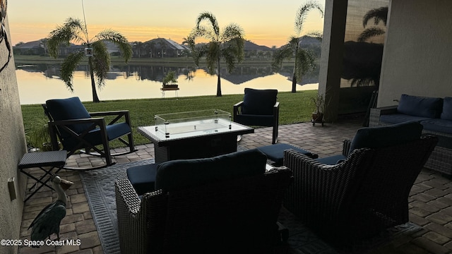 patio terrace at dusk with a water view, outdoor lounge area, and a lawn