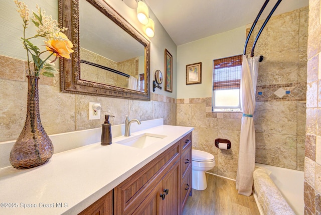 full bathroom with shower / tub combo with curtain, hardwood / wood-style flooring, tile walls, vanity, and toilet