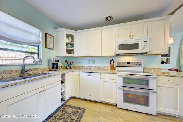 kitchen with sink, white cabinetry, light stone counters, white appliances, and light hardwood / wood-style floors