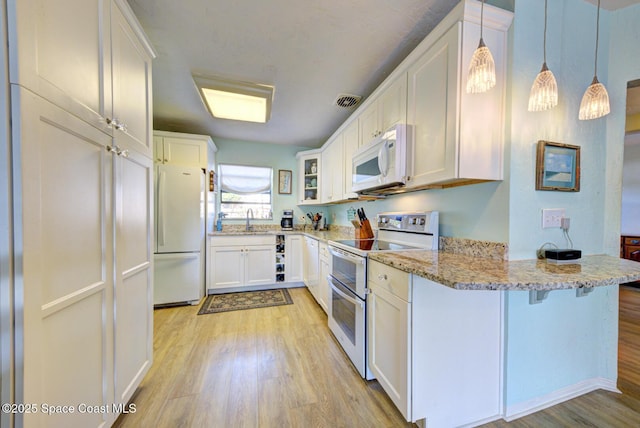 kitchen featuring sink, white cabinetry, light stone counters, hanging light fixtures, and white appliances