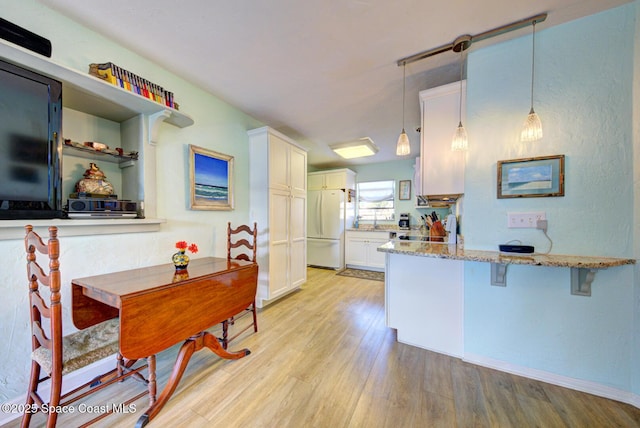 kitchen with white cabinetry, decorative light fixtures, kitchen peninsula, white fridge, and light hardwood / wood-style floors