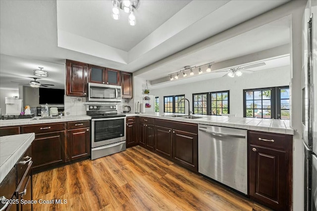 kitchen with sink, dark wood-type flooring, stainless steel appliances, tile countertops, and kitchen peninsula