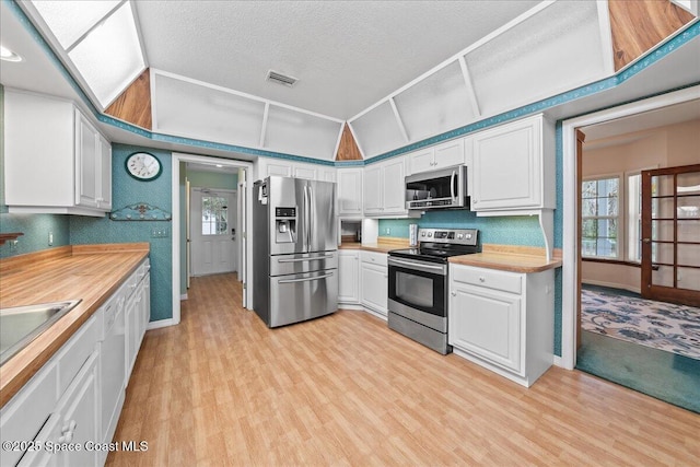 kitchen with lofted ceiling, appliances with stainless steel finishes, light hardwood / wood-style floors, and white cabinets