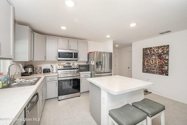 kitchen with sink, light tile patterned floors, gray cabinets, appliances with stainless steel finishes, and a kitchen bar