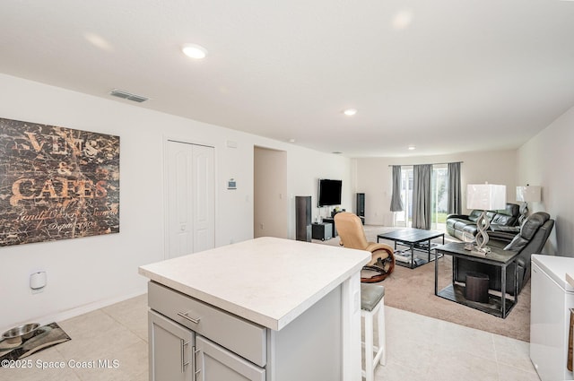 kitchen with light tile patterned flooring, a kitchen island, washer / dryer, a breakfast bar area, and gray cabinetry