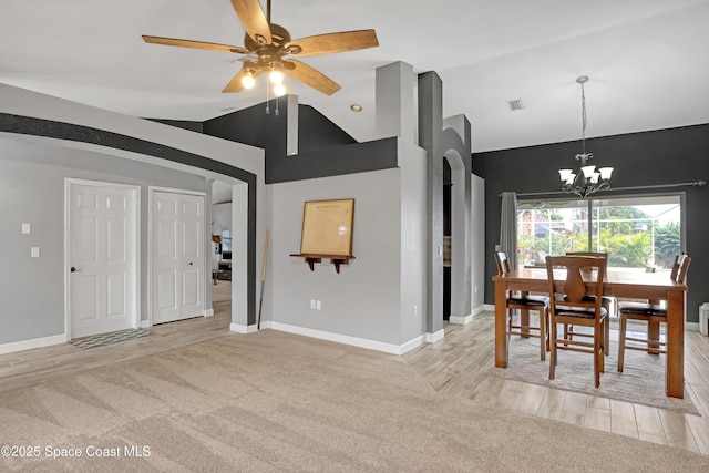 dining room with ceiling fan with notable chandelier, high vaulted ceiling, and light carpet