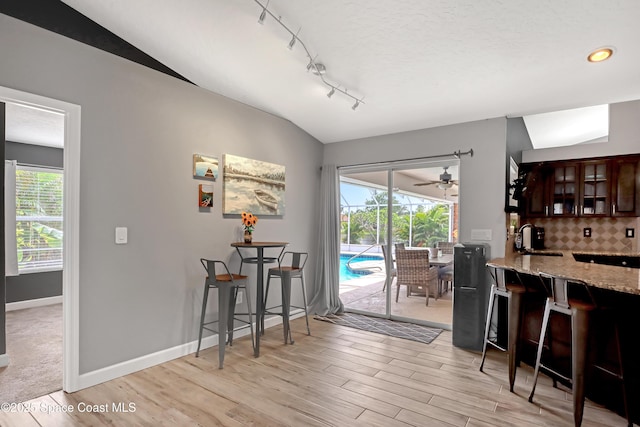 dining space with sink, vaulted ceiling, light hardwood / wood-style floors, and track lighting