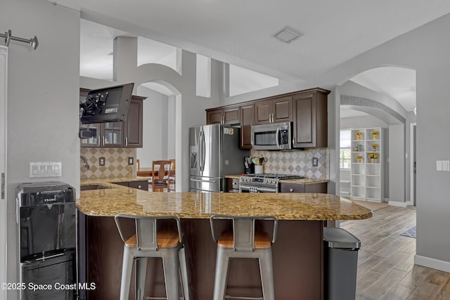 kitchen featuring a breakfast bar, backsplash, kitchen peninsula, stainless steel appliances, and light stone countertops