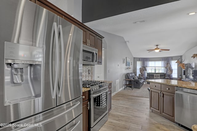 kitchen with lofted ceiling, light stone counters, dark brown cabinetry, stainless steel appliances, and light wood-type flooring