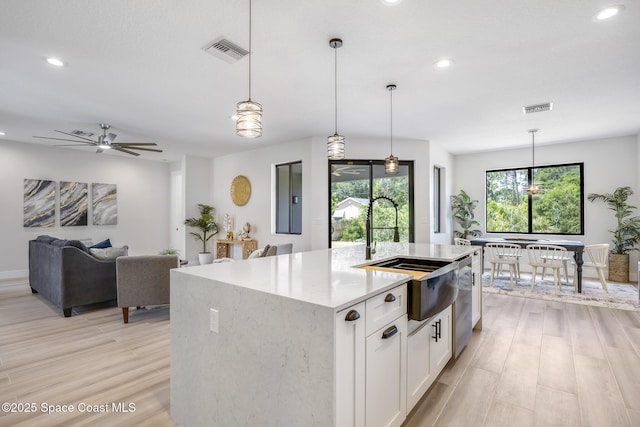 kitchen featuring hanging light fixtures, sink, an island with sink, and white cabinets