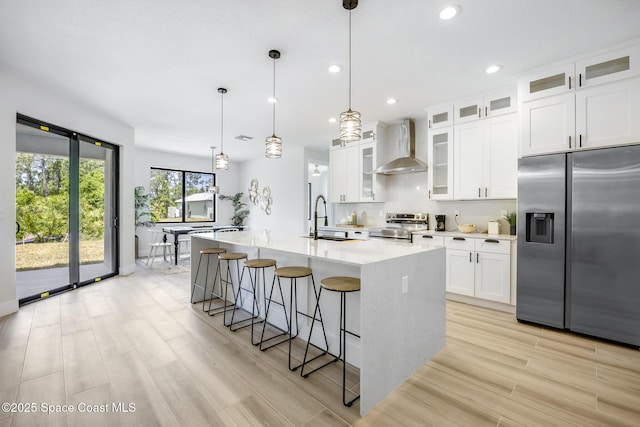 kitchen featuring an island with sink, appliances with stainless steel finishes, wall chimney range hood, and white cabinets