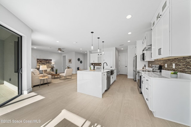 kitchen with a center island with sink, hanging light fixtures, white cabinets, stainless steel appliances, and backsplash