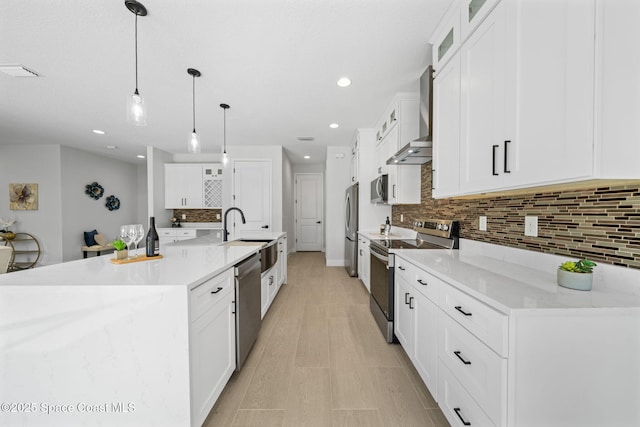 kitchen featuring white cabinetry, hanging light fixtures, wall chimney exhaust hood, stainless steel appliances, and a spacious island