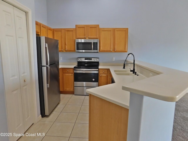 kitchen with light tile patterned floors, a peninsula, stainless steel appliances, light countertops, and a sink