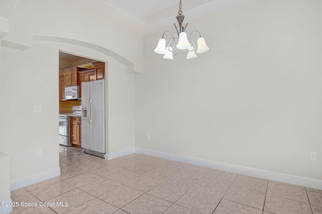 empty room with a tray ceiling, a chandelier, and light tile patterned floors