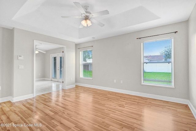 spare room featuring a raised ceiling, ceiling fan, and light hardwood / wood-style flooring