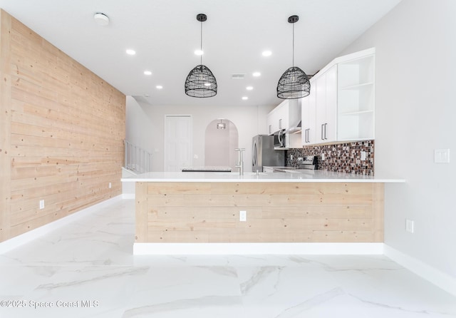 kitchen featuring appliances with stainless steel finishes, white cabinetry, hanging light fixtures, kitchen peninsula, and wood walls